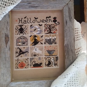 Pode incluir: Um sampler de ponto cruz emoldurado com tema de Halloween. O sampler apresenta vários ícones de Halloween, incluindo uma aranha, uma bruxa, um fantasma e uma abóbora. A palavra "Halloween" é costurada no topo. A moldura é de madeira envelhecida.