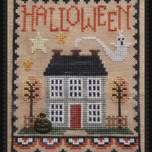 May include: Cross-stitch design featuring a house with a black roof, gray walls, and a red door. The word "HALLOWEEN" is stitched across the top. A ghost, pumpkin, and fall trees complete the festive scene.