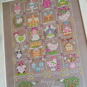 Pode incluir: Um sampler de ponto cruz com fundo castanho claro que apresenta 20 desenhos diferentes com tema de Páscoa. Os desenhos incluem coelhos, pintinhos, ovos, flores e outros motivos primaveris. O sampler é emoldurado em branco e tem o texto "Cuore e Batticuore" e "Happy easter!" bordado nos cantos inferiores.