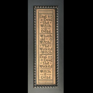 Könnte beinhalten: Ein gerahmter Kreuzstich-Sampler mit schwarzem Text auf beigefarbenem Hintergrund. Der Text lautet "Ding Dong the Witch is Dead. Which old Witch? The Wicked Witch. Ding Dong the Wicked Witch is Dead."
