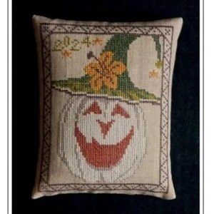 May include: A decorative, rectangular pillow with a cross-stitch design featuring a smiling pumpkin wearing a green witch hat. The pumpkin has a red-orange mouth and is framed by a decorative border. The text "2024" is stitched above the hat.