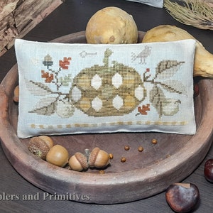 Puede incluir: Una almohada blanca con una calabaza marrón y blanca, hojas y bellotas bordadas en ella. La almohada está sentada en una bandeja de madera con bellotas y calabazas alrededor.