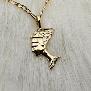 Puede incluir: Un collar de cadena de oro con un colgante que presenta un perfil detallado de una reina egipcia con un tocado.