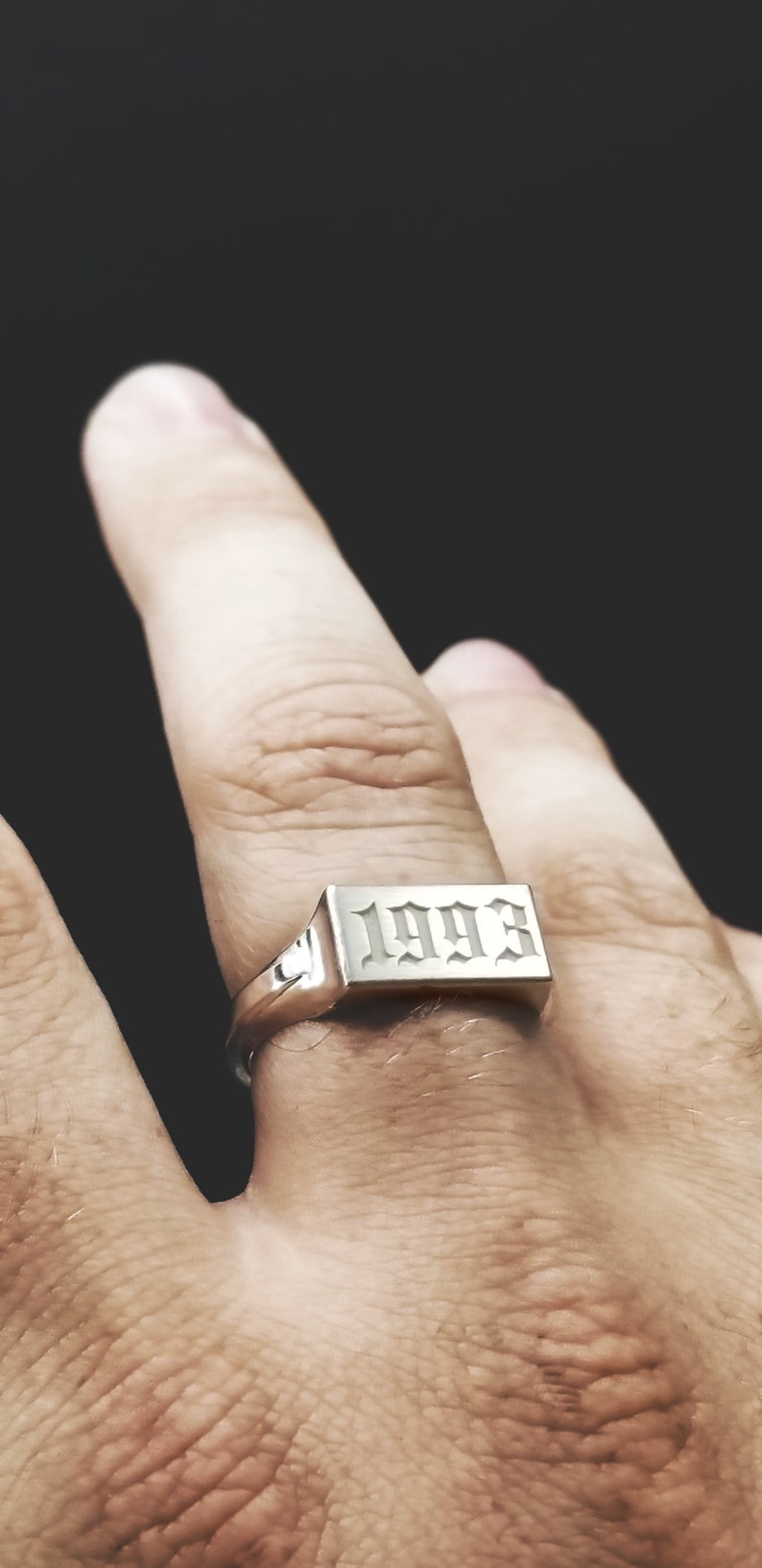 Peut inclure: Une bague en argent avec une bande rectangulaire grav&eacute;e de l'ann&eacute;e 1993 en police gothique.