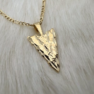 May include: A gold chain necklace with a textured arrow pendant.