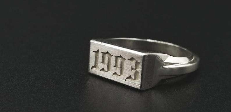 Peut inclure: Une bague signet en argent avec un dessus rectangulaire grav&eacute; de l'ann&eacute;e 1993 en police gothique.