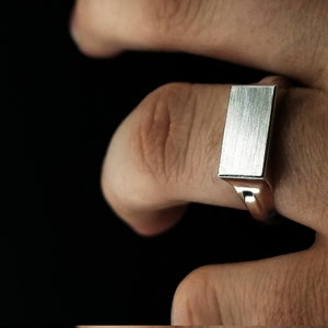 Peut inclure: Une bague signet en argent avec un dessus rectangulaire en m&eacute;tal bross&eacute;.