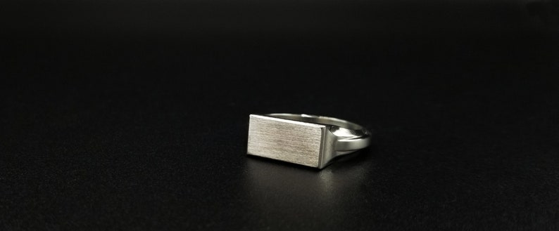 Peut inclure: Une bague signet en argent avec un dessus rectangulaire. Le dessus de la bague a une finition bross&eacute;e.