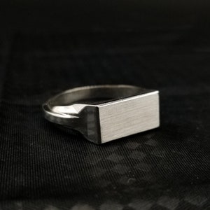 Peut inclure: Une bague signet en argent avec un dessus rectangulaire. Le dessus de la bague a une finition bross&eacute;e.