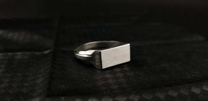 Peut inclure: Une bague signet en argent avec un dessus rectangulaire. Le dessus de la bague a une finition bross&eacute;e.