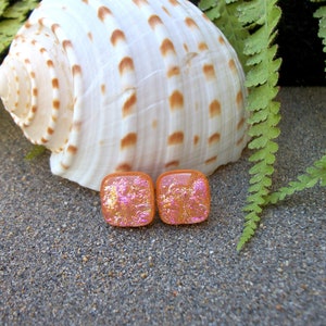 May include: Two square-shaped earrings with a pink and orange iridescent finish. The earrings are made of glass and have a textured surface.
