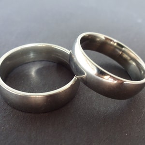 May include: Two silver wedding bands, one slightly larger than the other, are stacked on top of each other.