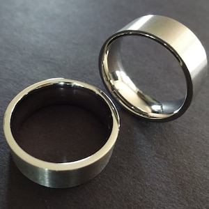 May include: Two silver wedding bands, one wider than the other, with a brushed finish.