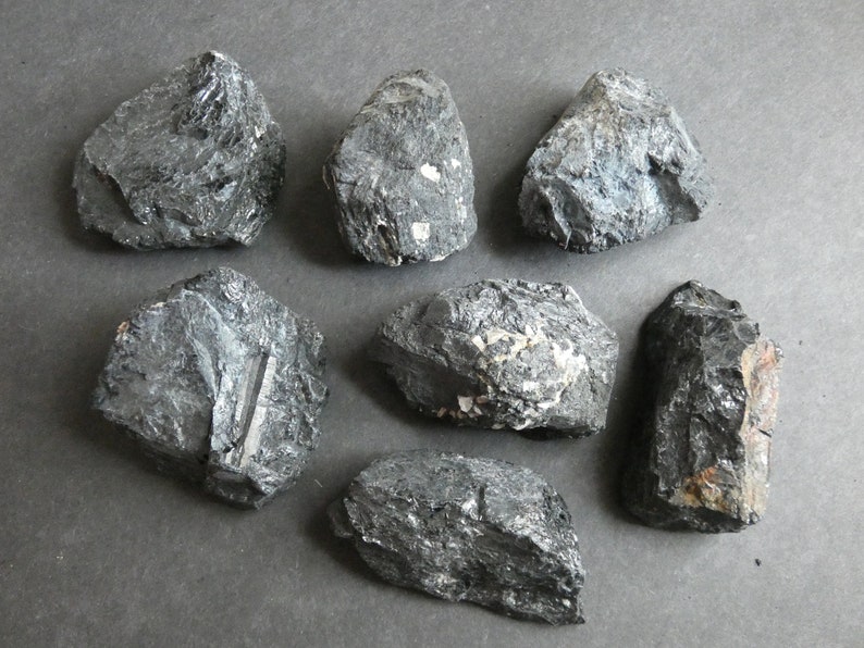 May include: Seven black, rough, and irregularly shaped stones. The stones have a dark, almost metallic sheen and some have white flecks.