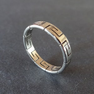 May include: A silver ring with a geometric pattern. The ring is made of metal and has a smooth finish.