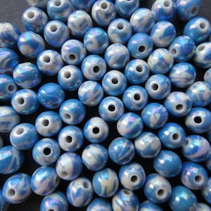 May include: A collection of blue and white iridescent glass beads. The beads are round and have a swirl pattern.