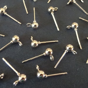 May include: A close-up of silver earring posts with a small ball at the end. The posts are arranged on a dark gray surface.