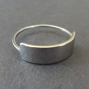 May include: A silver ring with a flat, rectangular band.