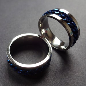 May include: Two silver rings with a blue chain design. The rings are stacked on top of each other.