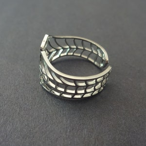 Op de afbeelding: Een zilveren ring met een geometrisch ontwerp. De ring is open en verstelbaar.