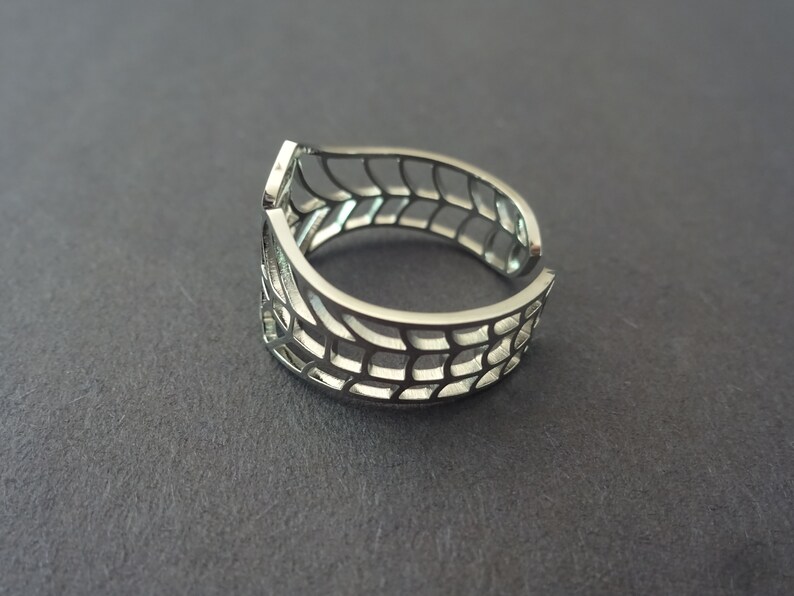 Op de afbeelding: Een zilveren ring met een geometrisch ontwerp. De ring is open en verstelbaar.