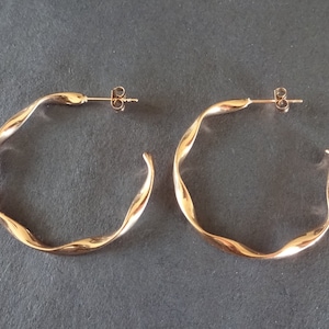 May include: A pair of gold-toned hoop earrings with a twisted design. The earrings are made of metal and have a simple, elegant style.