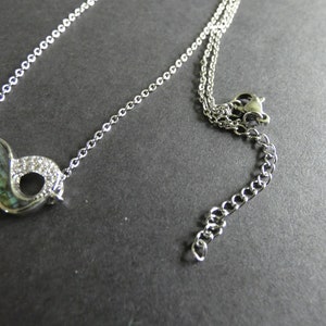 May include: A silver infinity symbol necklace with a mother-of-pearl inlay and clear rhinestones. The necklace has a silver chain with a lobster clasp.