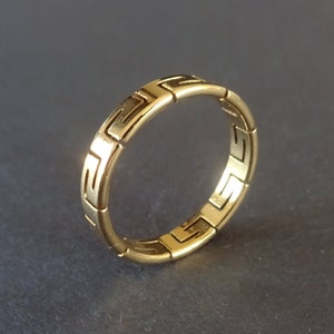 May include: A gold band ring with a geometric pattern. The ring is made of interlocking squares.