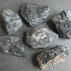 May include: A collection of seven black, rough, and irregularly shaped stones. The stones have a dark, almost metallic sheen.