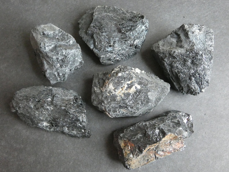 May include: A collection of seven black, rough, and irregularly shaped stones. The stones have a dark, almost metallic sheen.