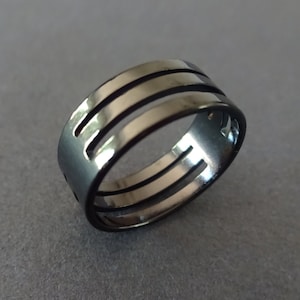 May include: A black metal ring with three horizontal bands cut out of the metal.