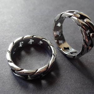 May include: Two silver rings with a braided design and cut-out details. The rings are stacked on top of each other.