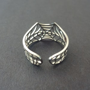 Op de afbeelding: Een zilveren ring met een webdesign. De ring is aan &eacute;&eacute;n kant open en heeft een delicaat, ingewikkeld ontwerp.