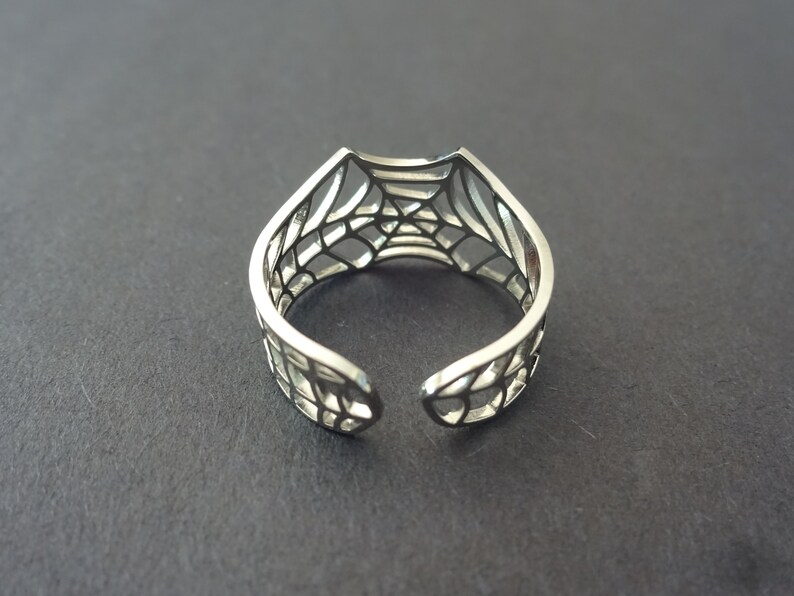 Op de afbeelding: Een zilveren ring met een webdesign. De ring is aan &eacute;&eacute;n kant open en heeft een delicaat, ingewikkeld ontwerp.
