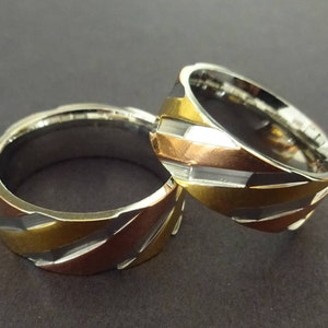 May include: Two silver rings with a gold and copper design. The rings have a textured, diagonal pattern.