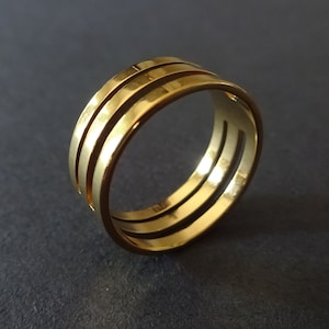 May include: A gold ring with three bands, each with a slightly different width. The ring is made of a smooth, shiny metal.