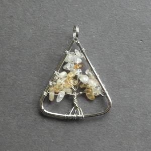 May include: A silver wire wrapped triangle pendant with a tree of life design. The tree is adorned with clear and amber colored stones.