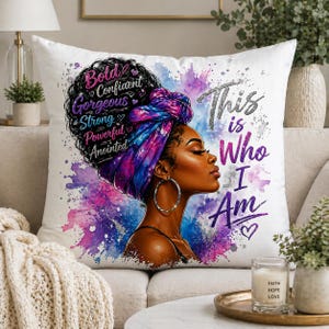 Op de afbeelding: Wit vierkant kussen met een zijaanzicht van een zwarte vrouw met een kleurrijke hoofddoek en grote oorringen. Het kussen heeft de tekst "Bold, Confident, Gorgeous, Strong, Powerful, Anointed" en "This is Who I Am."