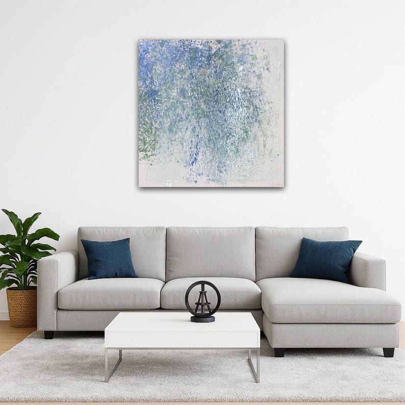 Pode incluir: Pintura abstrata com pinceladas azuis, verdes e brancas. A obra de arte est&aacute; pendurada acima de um sof&aacute; seccional cinza com almofadas azul marinho. Uma mesa de centro branca com estrutura de metal e uma est&aacute;tua decorativa da Torre Eiffel est&atilde;o em frente ao sof&aacute;.