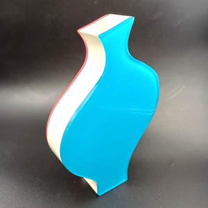 May include: A decorative vase with a distinctive, curved form. The vase showcases a vibrant colour scheme, with a bright blue exterior, a white central stripe, and a pink accent. The vase has a modern, artistic aesthetic.