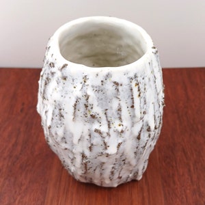 以下が含まれることがあります： 木の皮のような質感のある白い陶器の花瓶。花瓶は開口部が広く、丸みを帯びた形をしています。