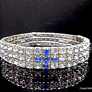 May include: A silver bracelet with multiple rows of clear rhinestones and a row of blue rhinestones in the centre.