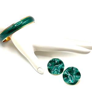 May include: A gold-toned bangle bracelet and matching earrings. The bracelet and earrings have a marbled emerald green enamel design. The earrings are round with a gold trim. The bracelet is on a white surface.