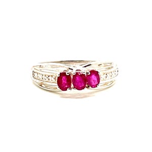May include: A silver ring featuring three oval-cut, vibrant red gemstones. The band is accented with small, clear stones. The ring's design is elegant and eye-catching, suitable for special occasions or everyday wear.