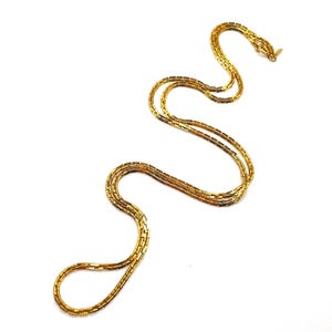 May include: A gold-toned chain necklace featuring a series of interconnected rectangular links that create a flexible, snake-like structure. The necklace is arranged in a winding, serpentine pattern and includes a small metal clasp at one end.