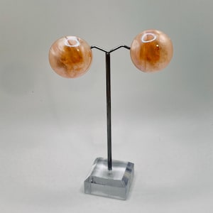 May include: A pair of peach and orange swirl resin earrings on a display stand.