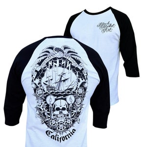 May include: A white and black baseball t-shirt with a black eagle, ship, skull, and candles graphic on the front. The text "EST. 1967 CORMAC TATTOOS" is in a circle around the graphic. The text "California" is below the graphic. The back of the shirt has the text "Black Market Art" in black on the white portion of the shirt.