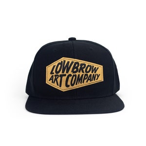 May include: Black baseball cap with a tan leather patch that says "Lowbrow Art Company" in black lettering.