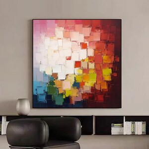 May include: Abstract painting with a colorful geometric pattern of squares in shades of red, orange, yellow, green, blue, and white. The painting is framed in black and has a textured, brushstroke effect.
