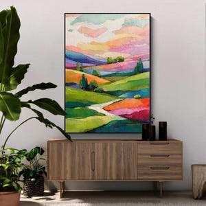 May include: A framed landscape painting with vibrant colors. The artwork depicts rolling hills in shades of green, orange, and purple, under a sky of pink, yellow, and blue. The painting is displayed above a wooden cabinet.